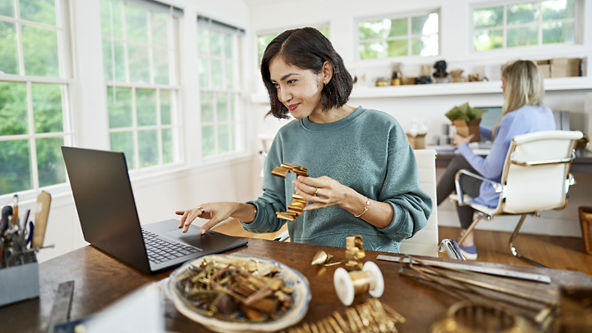 Female holding a metal craft as she works on her laptop in an office