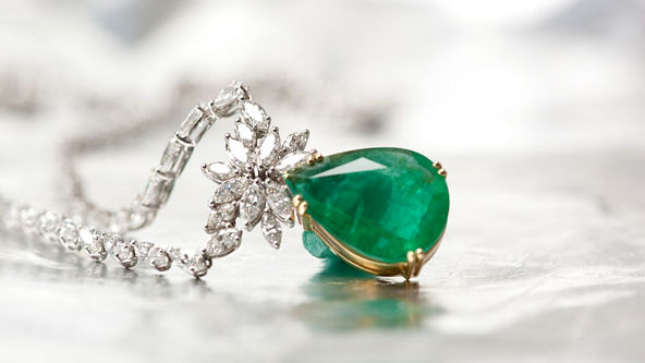 Close up of a green gemstone and diamond necklace on silver background