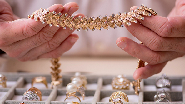 Hands holding a gold and diamond necklace over a try of gold rings