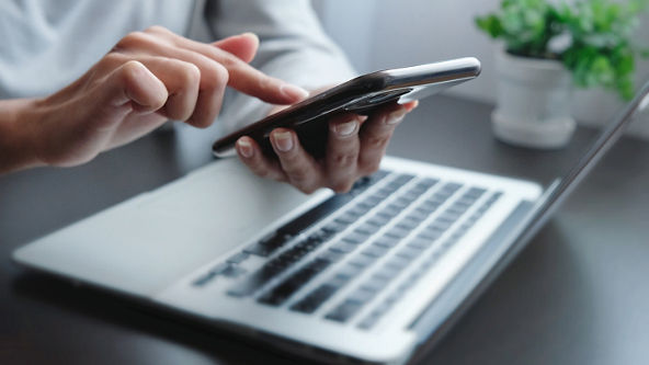 Close up of hands using a smart phone by a laptop