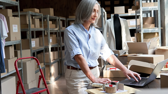 Female using a laptop in a store room full of boxes 