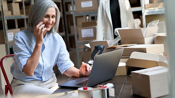 Female talking on her phone and using her laptop in a store room full of boxes