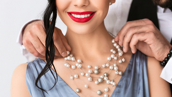Male placing a pearl necklace on the neck of a female 