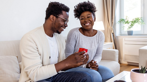 Male giving a red ring box to a female in their living room