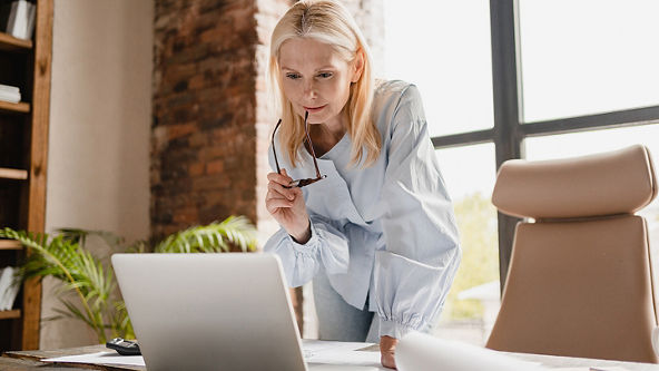 Female holding her glasses and leaning down to look at her laptop