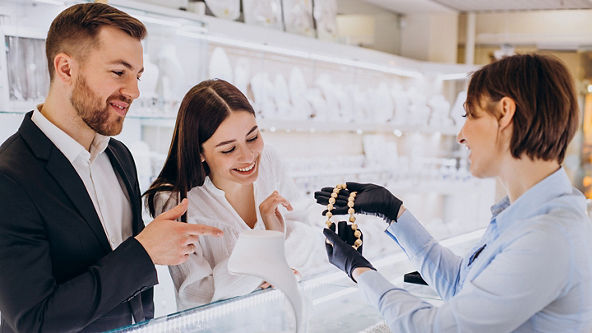 A jewelry store sales woman showing a couple a gold necklace