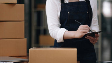 Woman writing something on pad of paper with box on counter