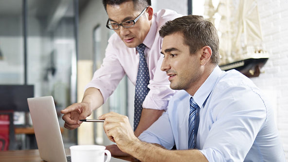 Two males pointing and looking at a laptop