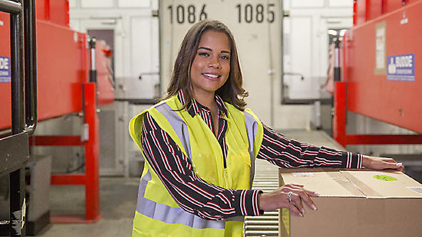 Female in a safety vest grabbing a box off a conveyer belt