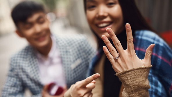 Female pointing to ring on finger with male in background