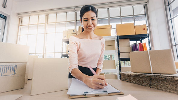 Female writing on a clipboard on a desk full of boxes 