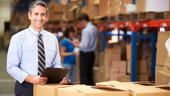 Male holding a clipboard and standing by boxes in a warehouse