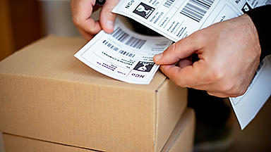 Close up of hands holding and placing a shipping label on a box 