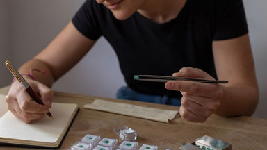 Female holding a green gemstone with tweezers and taking notes 