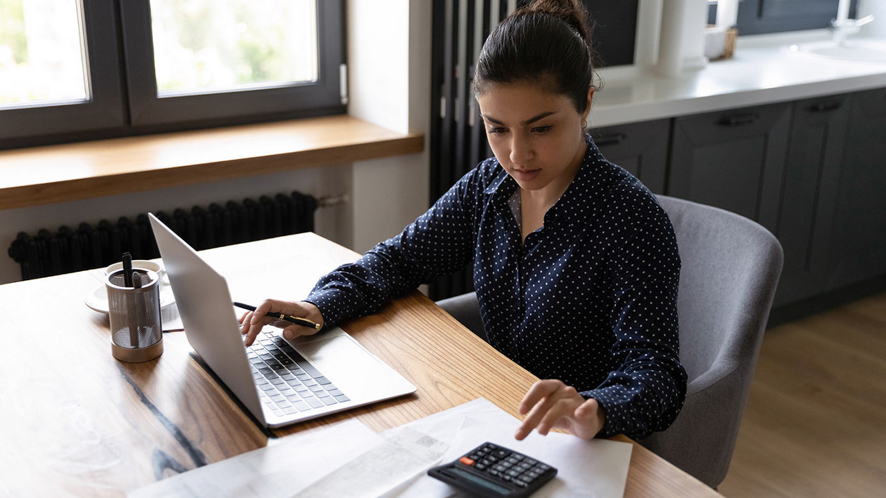Woman working on laptop and entering figures into calculator