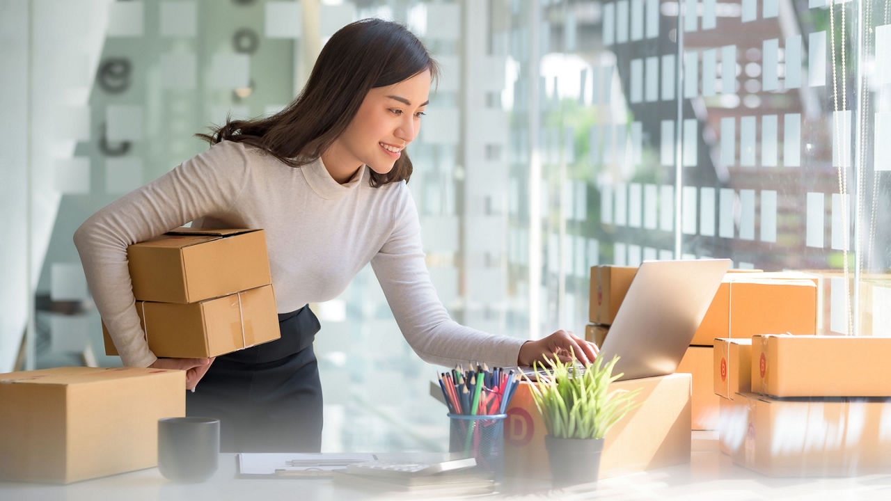 Female holding two packages and using her laptop 