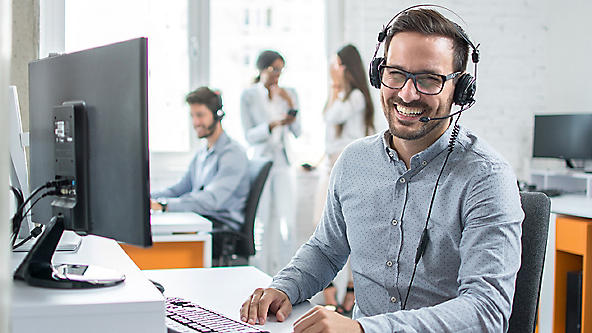 Male wearing a headset at a computer in an office