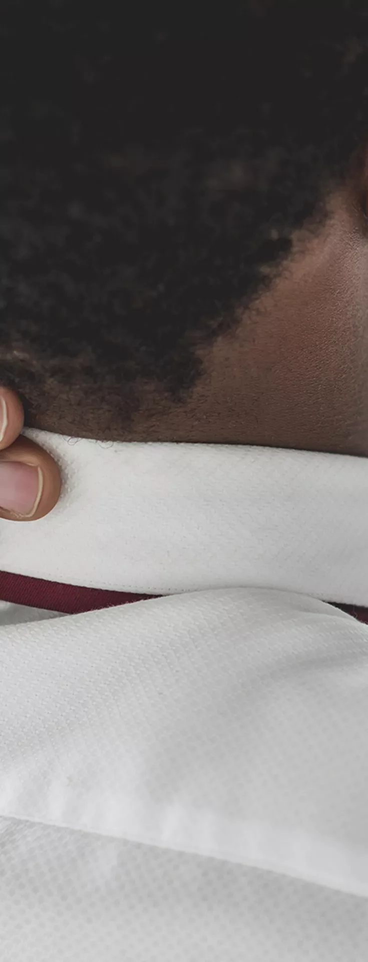 A man in a white shirt is seen from behind, holding his neck as if experiencing discomfort. He is seated at a desk with a smartphone in one hand and a laptop in the background. The setting suggests an office environment, with a focus on workplace stress or fatigue. The overall palette is neutral and professional.
