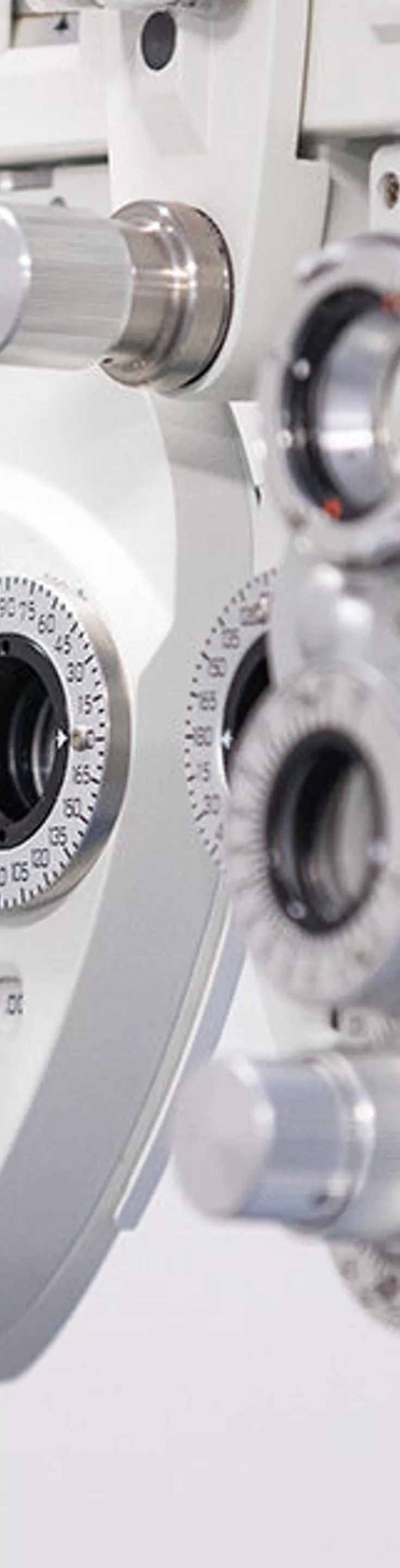 A detailed view of a phoropter, an essential device used in eye examinations to measure refractive error and determine eyeglass prescriptions. The equipment is shown in a clinical setting with a clean, neutral background, highlighting its metallic dials and lenses. The image focuses on the intricate mechanical components, emphasizing precision and advanced technology. No visible text or numbers are present on the device.