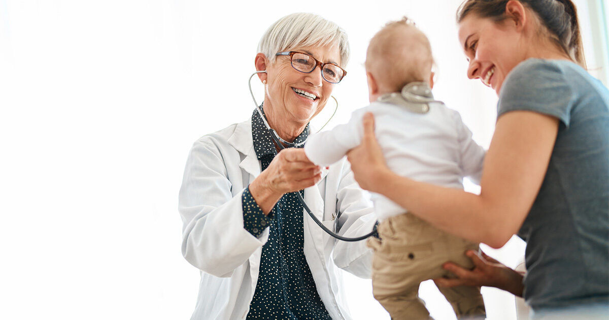 A healthcare professional uses a stethoscope to examine a baby held by an adult in a bright medical office. The scene highlights a routine pediatric checkup, with the doctor wearing a white coat and the baby dressed in light clothing. The setting is clean and clinical, emphasizing care and trust. The overall mood is calm and professional.