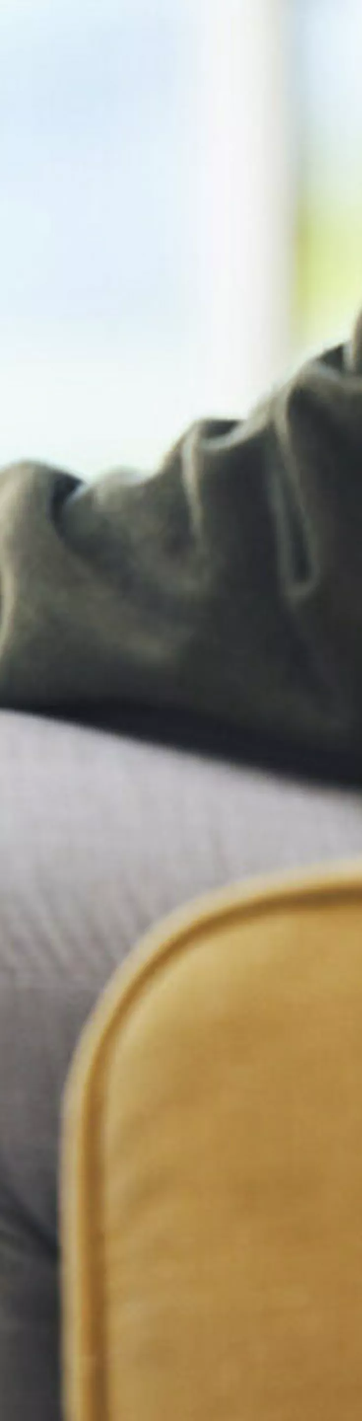 The image shows two adults seated in comfortable chairs, engaged in a conversation. One person gestures with their hand while the other sits with hands clasped, suggesting an attentive or thoughtful exchange. The setting appears to be a professional or therapeutic environment, with warm lighting and neutral tones. No visible text or numbers are present in the image.