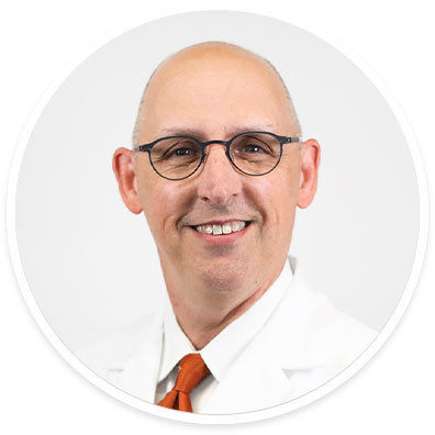 A middle-aged male is pictured wearing a white coat and an orange tie, suggesting a professional or medical setting. The background is plain white, emphasizing a clean and clinical environment. The subject's attire and neutral palette convey a formal and authoritative mood. No visible text or numbers are present in the image.