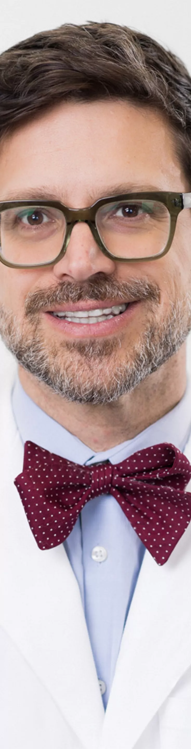 Headshot of Alex Haynes. He is wearing a blue dress shirt, red bowtie, and a white coat.