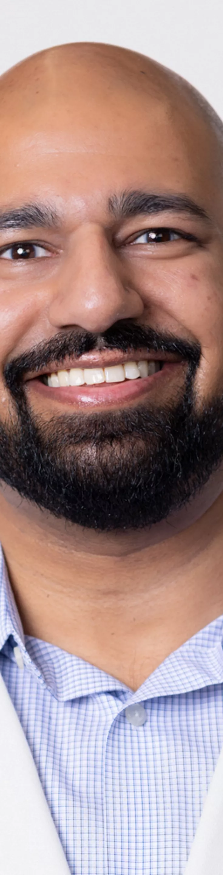 Headshot of Aman Mittal. He is wearing a blue dress shirt and a white coat.