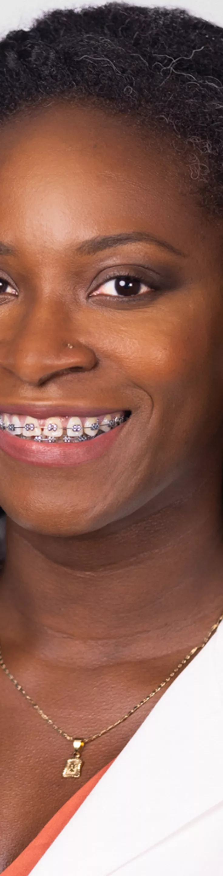 Headshot of Audrey Addaquay-Corey. She is wearing an orange blouse and a white coat.