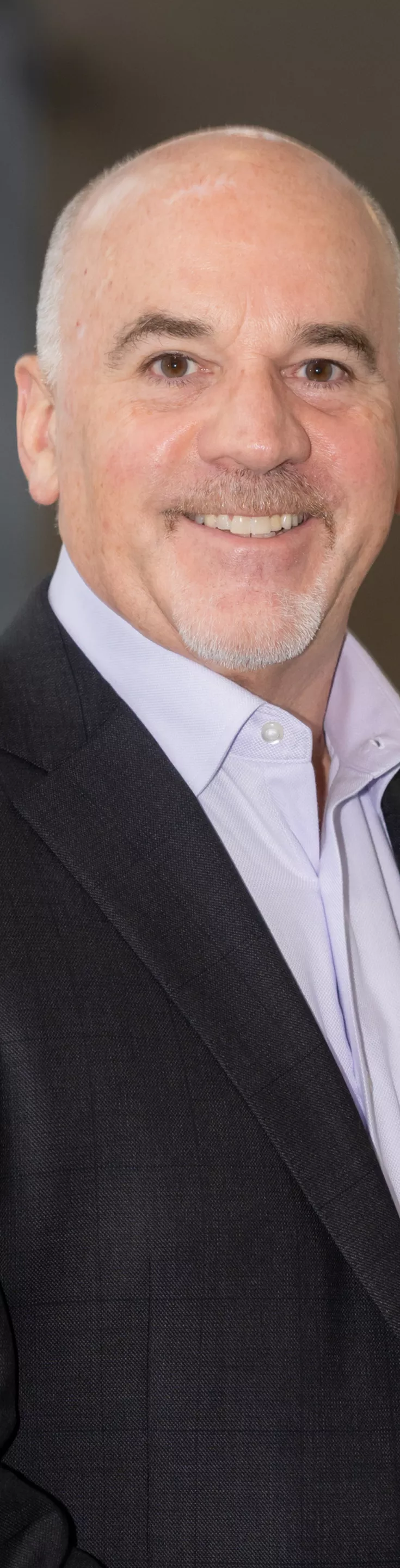 Headshot of Charles Taylor. He is wearing a light purple dress shirt and a black blazer. The background features glass walls and soft natural light, creating a professional and neutral atmosphere.