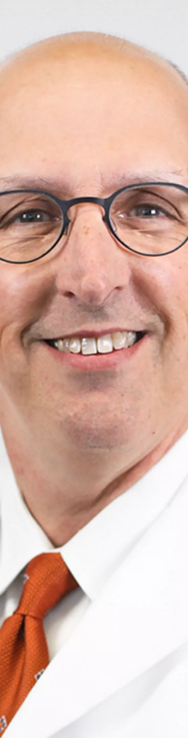 Headshot of Declan Fleming. He is wearing a whtie dress shirt, orange tie, and a white coat.