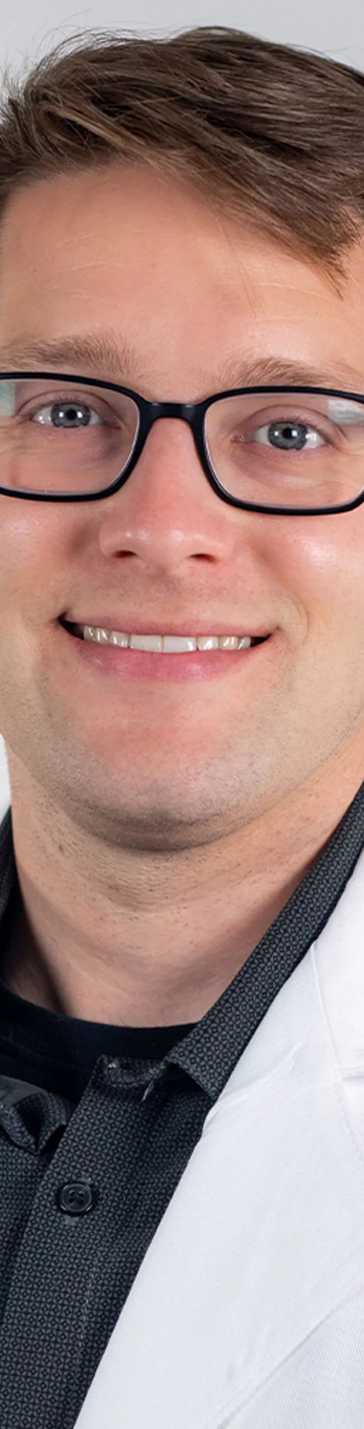 Headshot of Eric Corwell. He is wearing a black dress shirt and a white coat.