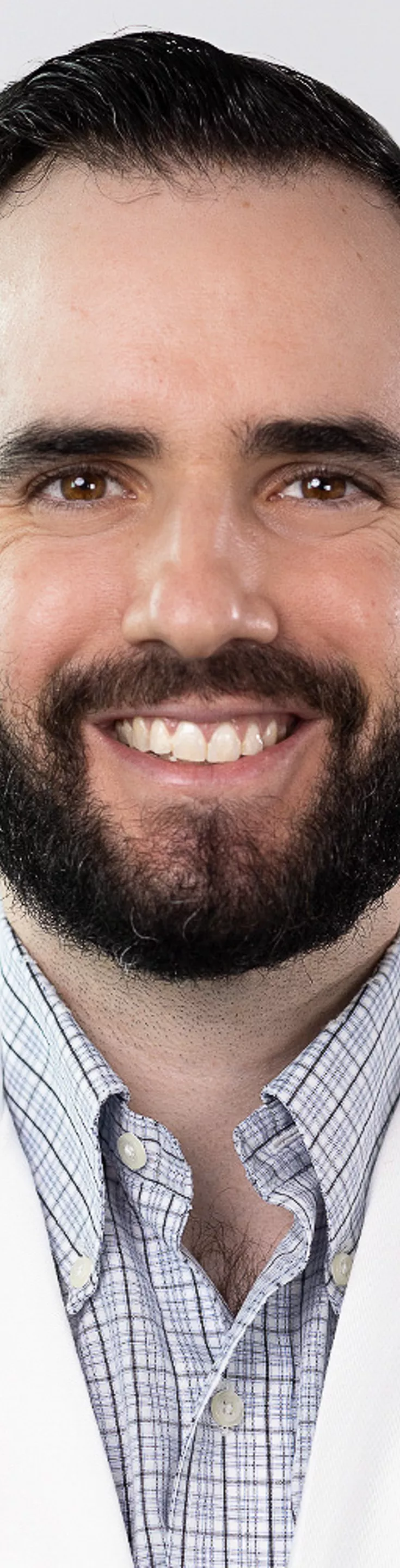 Headshot of Ethan Meltzer. He is wearing a blue plaid dress shirt and a white coat.