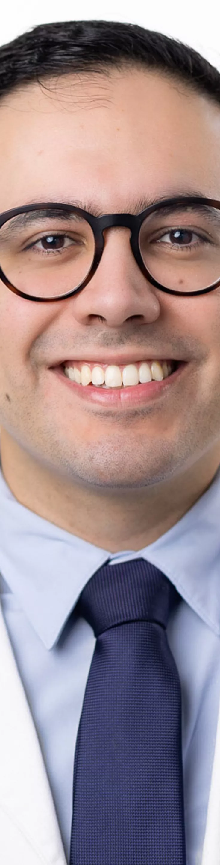Headshot of Felipe Flores. He is wearing a blue dress shirt, a blue tie, and a white coat.
