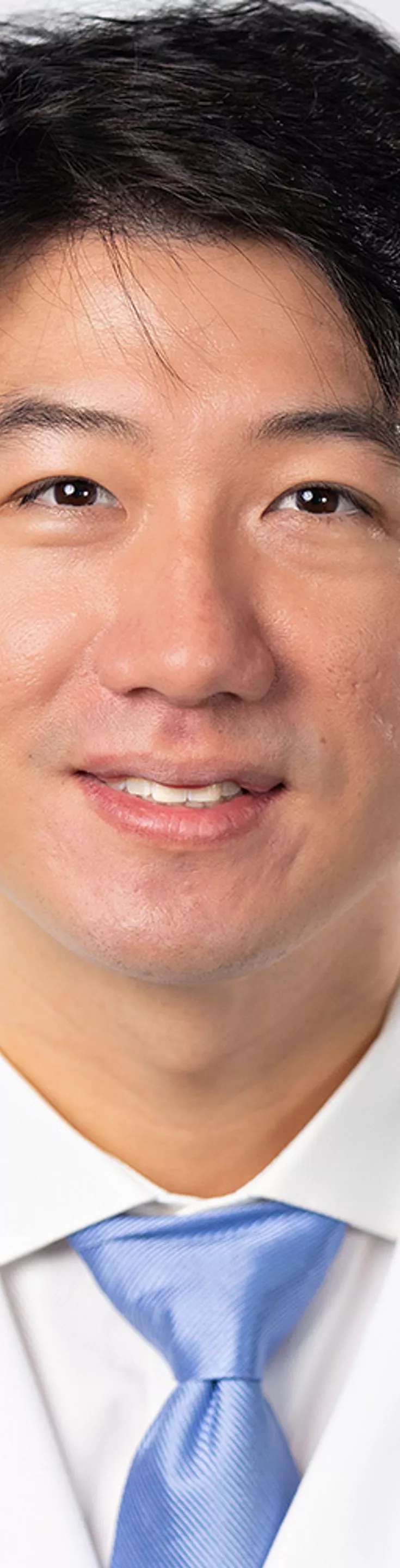 Headshot of Gene Kim. He is wearing a white dress shirt, blue tie, and a white coat.