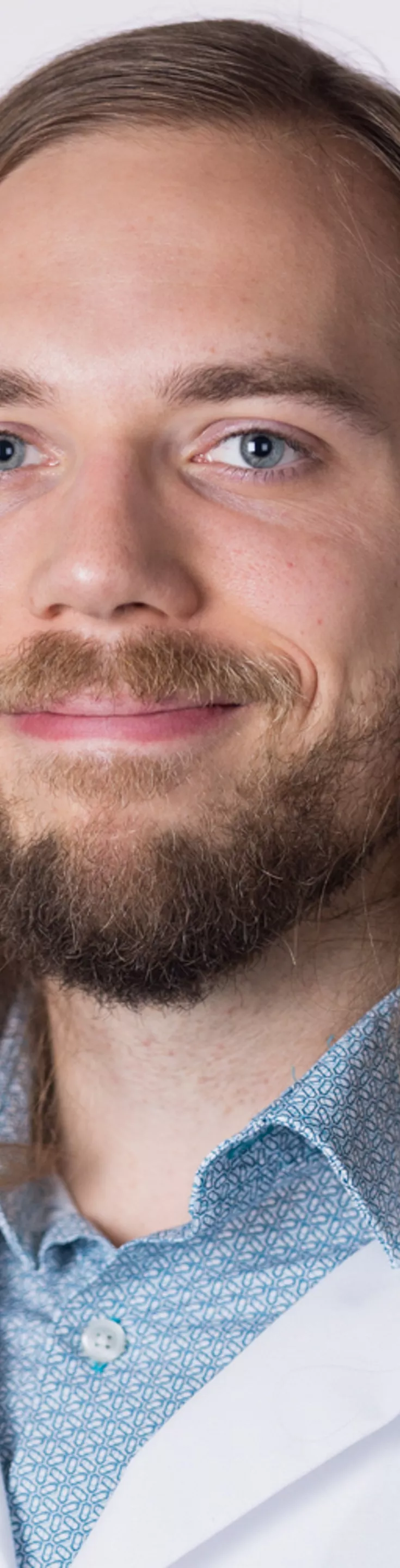 Headshot of Gregory Muller. He is wearing a blue dress shirt and a white coat.
