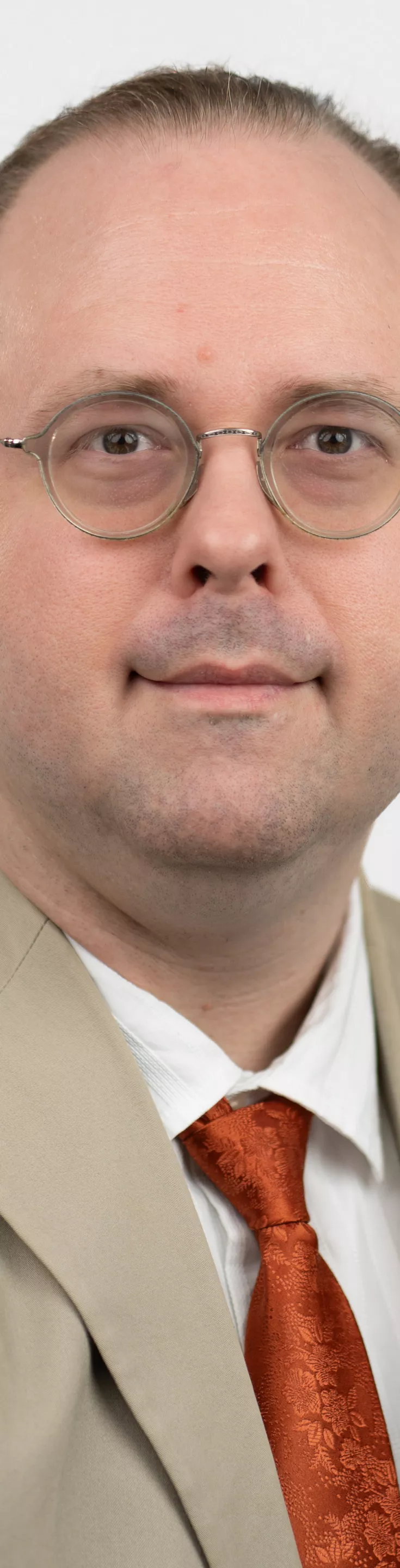 Headshot of James Burns. He is wearing a white dress shirt, an orange tie, and a tan suit.