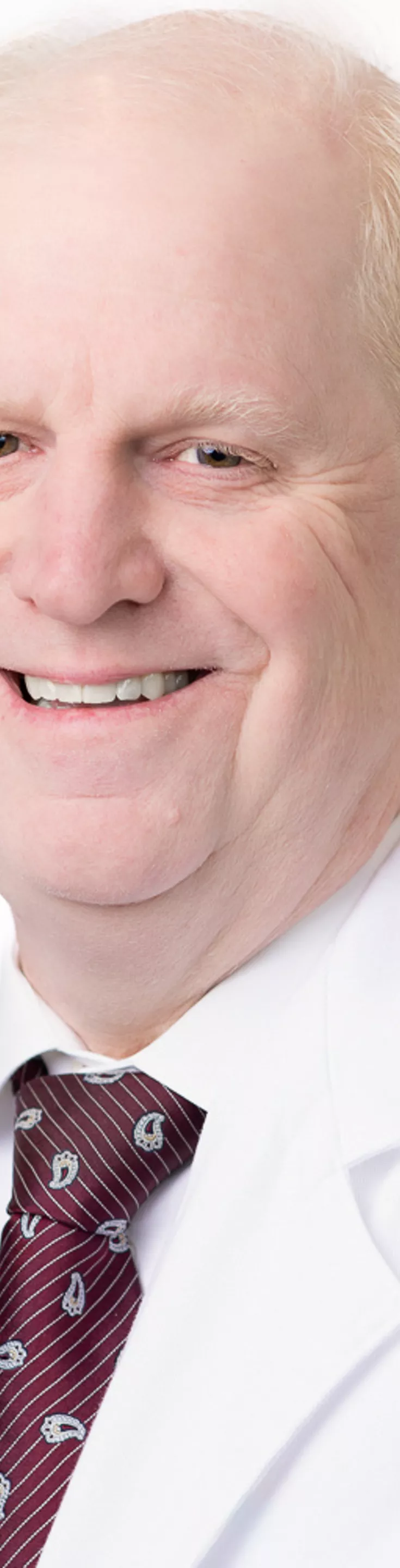Headshot of James Korndorffer. He is wearing a white shirt, red tie, and a white coat.
