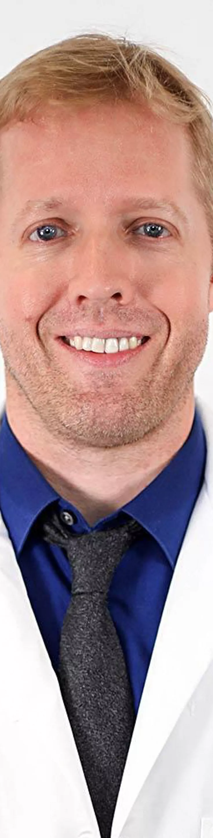 Headshot of John Bertelson. He is wearing a blue dress shirt, a black tie, and a white coat.