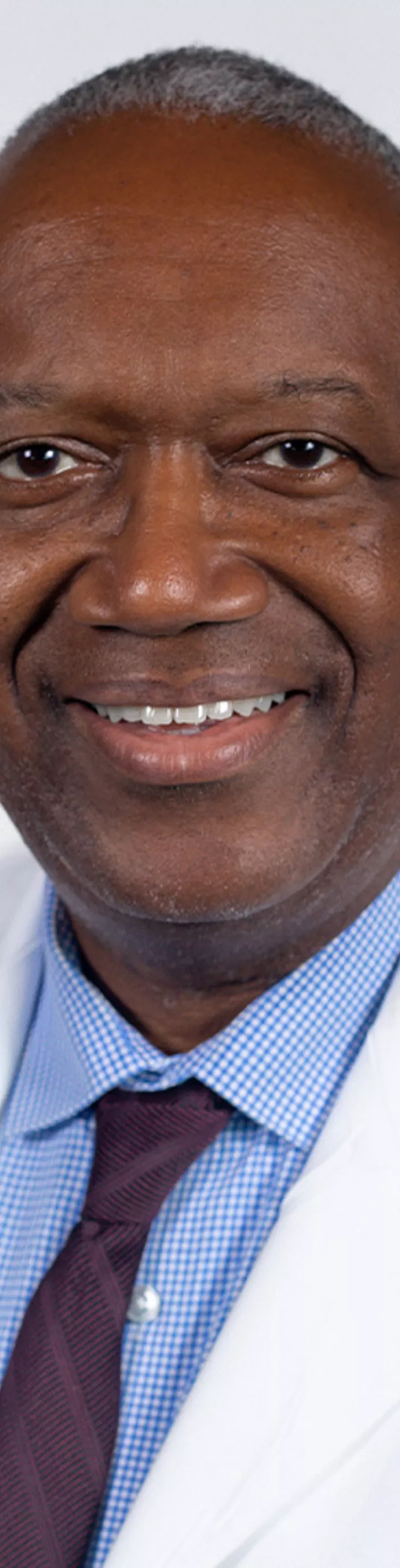 Headshot of Kevin Hackshaw. He is wearing a blue dress shirt, purple tie, and a white coat.