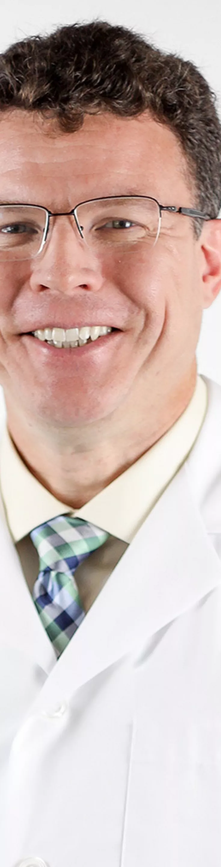 Headshot of Jonathan MacClements. He is wearing a white coat, yellow shirt, and a blue tie.
