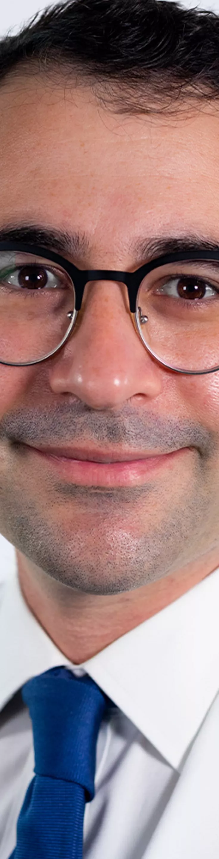 Headshot of Max Holtz. He is wearing a white dress shirt, a navy tie, and a white coat.