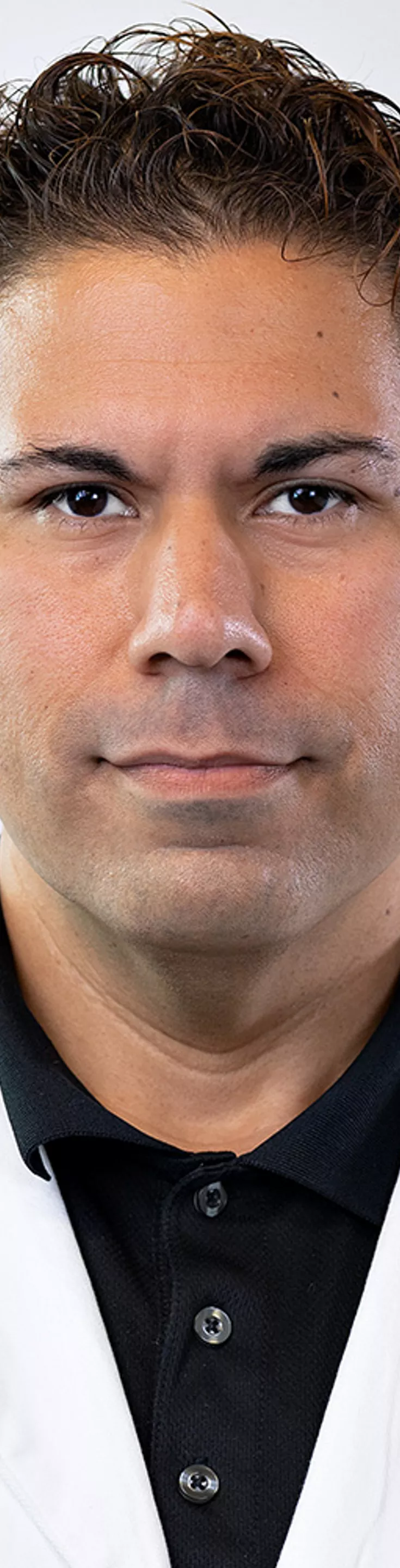 Headshot of Mica Guzman. He is wearing a black polo and a white coat.