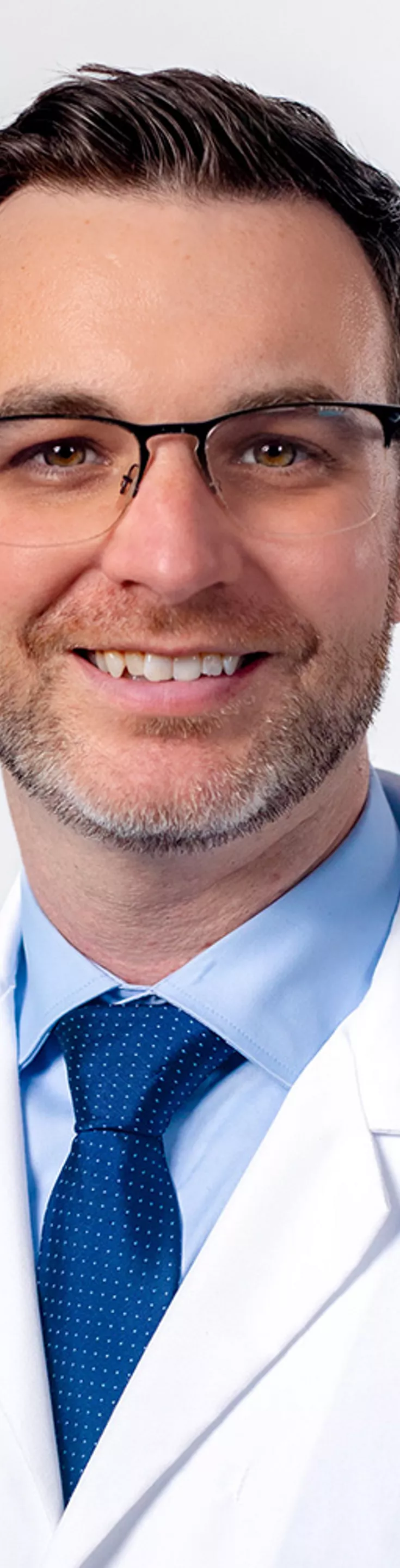 Headshot of Michael Brode. He is wearing a blue dress shirt, a blue tie, and a white coat.