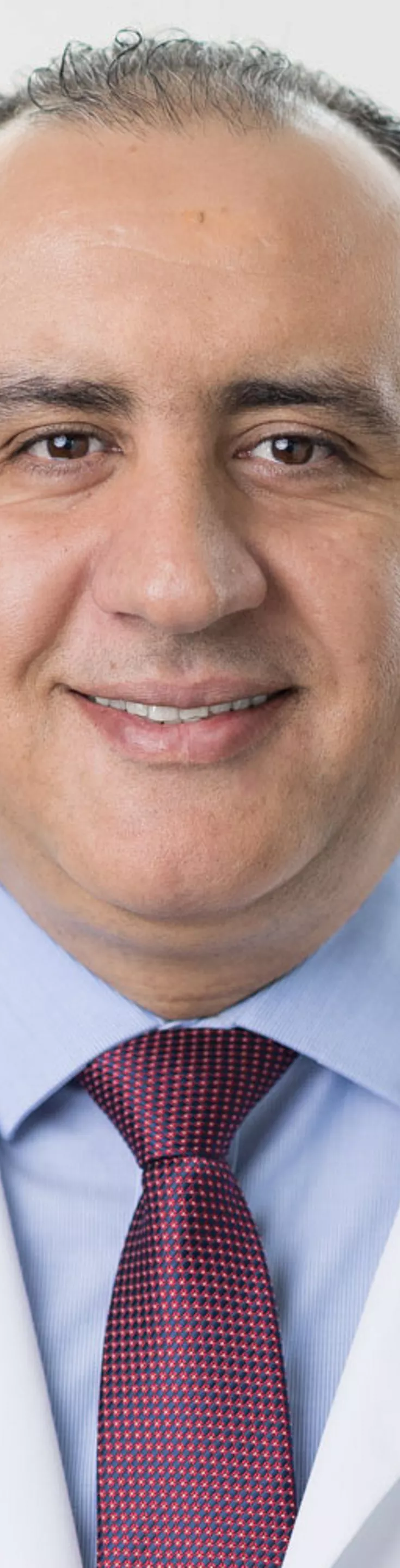 Headshot of Mohammad Alsumrain. He is wearing a blue dress shirt, a red tie, and a white coat.