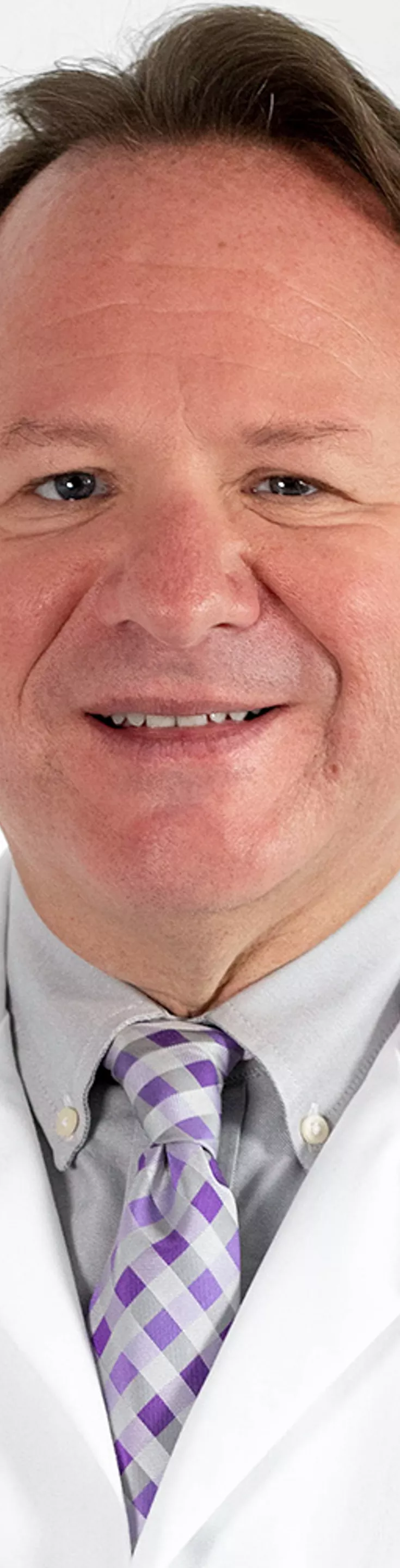 Headshot of Jeffrey Newport. He is wearing a blue shirt, purple tie, and a white coat.