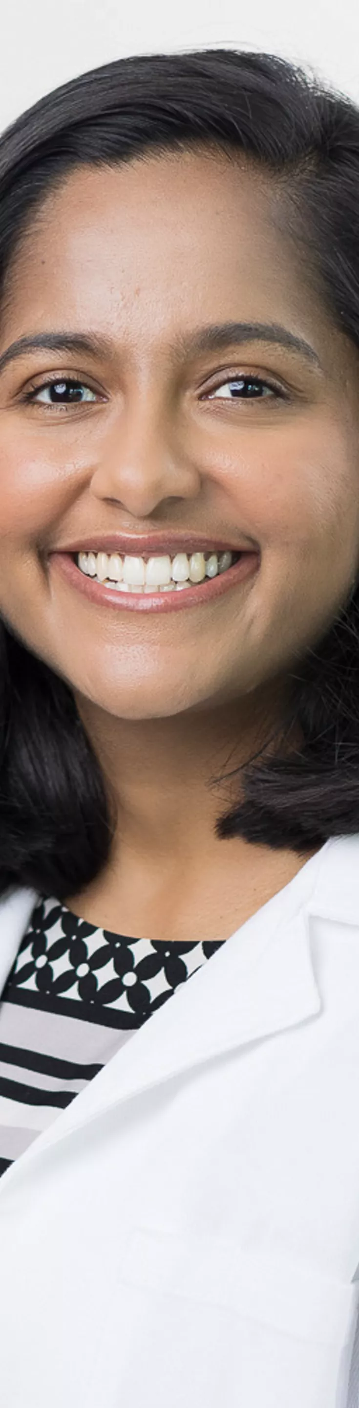 Headshot of Nimmy Thomas. She is wearing a black and white blouse and a white coat.
