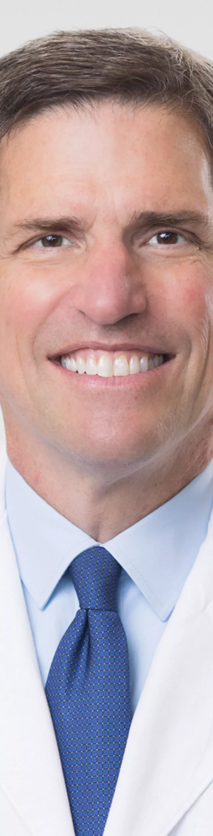 Headshot of Paul Mueller. He is wearing a blue dress shirt, blue tie, and a white coat.