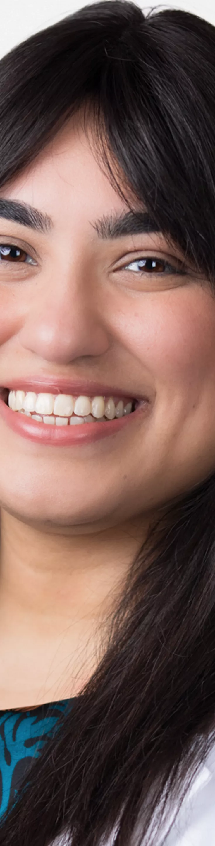 Headshot of Priya Kumar-Kaparaboyna. She is wearing a blue and black floral blouse and a white coat.