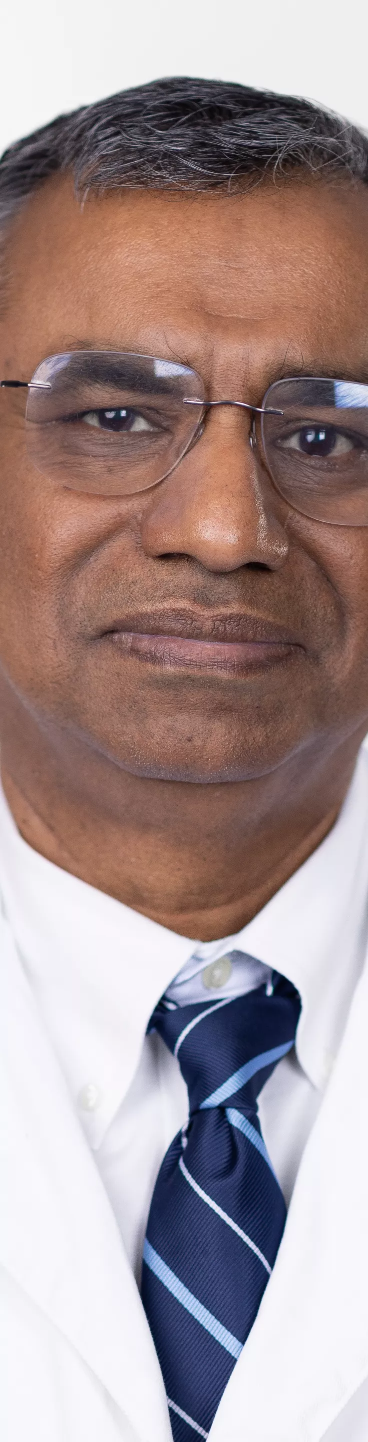 Headshot of Rumi Khan. He is wearing a navy striped tie, a white dress shirt, and a white coat.